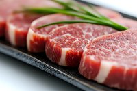 Fresh raw marbled beef steaks arranged on black stone plate with green onion garnish, showing rich meat texture and natural fat marbling pattern.