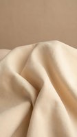 Soft beige linen fabric with natural folds and wrinkles creating elegant drapery against neutral background for textile and fashion design projects.