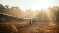 Tennis court at golden hour with net and sunlight creating warm atmosphere for sports and recreation activities.