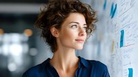Professional businesswoman with curly hair analyzing data charts and graphs on office whiteboard for strategic planning and market research.
