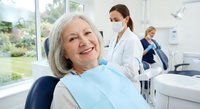 Senior Caucasian woman smiling during dental checkup with female dentist in modern clinic office. Professional healthcare and oral hygiene consultation.