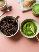 Coffee beans and matcha powder in bowls with traditional bamboo whisk on pink background. Healthy beverage ingredients for cafe menu and cooking.