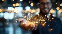 Young Asian businessman holding magical glowing golden sparkles in palm against blurred bokeh background, representing success and innovation in business.