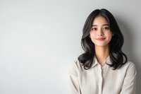 Young Asian woman with long dark hair wearing white shirt smiling confidently against light background. Professional portrait with copy space for business concepts.