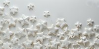 White meringue stars scattered on light background creating festive border pattern. Sweet holiday confectionery composition for dessert decoration and celebration designs.