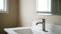 Modern stainless steel faucet on white bathroom sink with neutral walls and natural light from windows, suitable for home design and renovation projects.