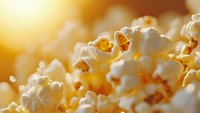 Fresh popcorn kernels in extreme macro shot with warm golden sunlight and soft bokeh background, showing detailed texture of fluffy white popped corn.