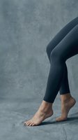 Woman legs in black leggings walking barefoot on concrete floor against textured gray wall background for fitness and wellness concepts.
