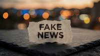 Torn paper with fake news text against blurred city lights background at dusk. Concept for misinformation, media literacy and journalism ethics.