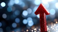 Red glittery arrow pointing upward against blurred bokeh background with sparkles and light effects, representing growth, success and positive direction.