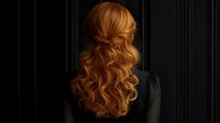 Back view of long wavy copper red hair styled with twisted crown detail against dark background, showcasing elegant feminine hairstyle for special occasions and bridal looks.