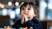 Young Asian girl in navy sequin dress clasps hands together while looking up with wonder, bokeh lights create magical atmosphere. For childhood, faith and dreams concepts.