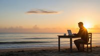Professional man working on laptop at beach desk during golden sunset with ocean waves for remote work and digital nomad lifestyle concepts.