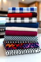 Stack of colorful folded textile fabrics with various patterns including plaid, checkered, and geometric designs for sewing, crafting, and home decor projects.