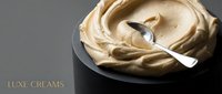 Luxurious beige cream swirl in black bowl with silver spoon on gray background, cosmetic skincare product for beauty and wellness applications.
