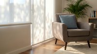 Modern beige armchair with blue cushion in bright living room with palm plant and natural sunlight streaming through window creating cozy atmosphere.