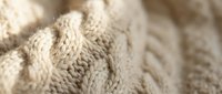 Cozy beige cable knit sweater texture with intricate braided pattern details for fashion and textile design projects.