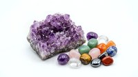 Amethyst crystal cluster with colorful gemstones including tiger eye, jade, carnelian and quartz arranged on white background for healing and meditation.
