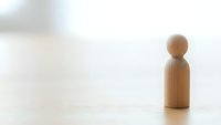 Wooden peg figure standing alone on light surface with soft blurred background representing solitude, minimalism, and individual concept for business presentations.