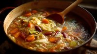 Homemade vegetable soup with beans, carrots, and cabbage simmering in copper pot with wooden spoon, warm comfort food for cold weather.
