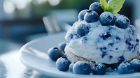Fresh blueberry dessert with whipped cream and ripe berries on white plate, macro food photography with soft natural lighting and bokeh background.