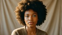 Young African American woman with natural curly afro hair wearing beige sweater against neutral background for lifestyle and beauty concepts.