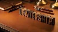 Leadership word spelled in vintage wooden letterpress blocks on a leather desk with pens, symbolizing business authority and success.
