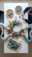 Group of people crafting festive wreath with eucalyptus, dried oranges and pinecones on white table with candles for holiday decoration workshop.