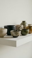Assorted ceramic bowls and vessels in neutral earth tones displayed on white platform with dried botanical element, showcasing handmade pottery for home decor and interior styling.