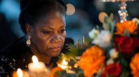 Elegant African American woman in formal attire with pearl earrings surrounded by colorful flowers and warm candlelight creating intimate atmosphere.