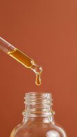 Golden amber serum or oil dripping from dropper pipette into glass bottle against warm terracotta background. Skincare, cosmetics, wellness product.