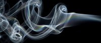 Iridescent smoke swirls with rainbow light reflections on a dark black background, creating an abstract, ethereal flow of motion and color.