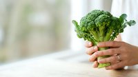 Fresh broccoli held in hands against blurred window background, promoting healthy eating and nutrition for cooking, recipes, and wellness content.