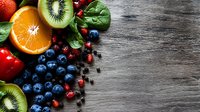 Fresh assorted fruits including kiwi, blueberries, strawberries, and citrus arranged on rustic wooden surface with copy space for food and wellness content.