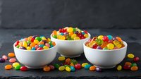 Colorful candy-coated chocolates in white ceramic bowls on dark background. Sweet confectionery treats for dessert, party celebration or snack time enjoyment.