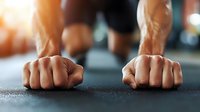 Close-up of muscular hands in plank position on gym floor during intense workout, showing strength and determination in fitness training session.