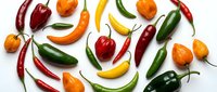 Colorful assortment of fresh hot chili peppers in red, green, yellow and orange varieties scattered on white background for culinary and cooking designs.