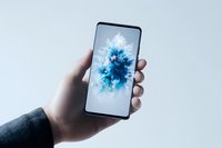 Hand holding modern smartphone displaying abstract blue explosion effect on white screen against light background. Suitable for tech advertising.