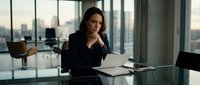 Professional businesswoman analyzing documents in modern corporate office with city skyline view during evening hours.