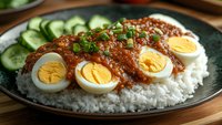 Spicy minced meat sauce served over steamed white rice with sliced boiled eggs, fresh cucumber and green onions garnish on dark plate. Traditional Asian cuisine.