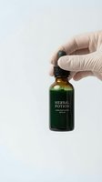 Hand in latex glove holding green herbal potion dropper bottle for natural medicine and wellness treatments on white background.