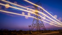 High voltage electrical transmission tower with dynamic light trails against twilight sky. Energy infrastructure and power grid concept for industrial projects.