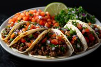 Mexican street tacos with seasoned ground beef, fresh pico de gallo, chopped cilantro, and lime on corn tortillas served on white plate against dark background.