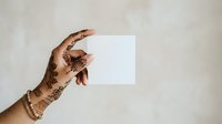 Female hand with henna mehendi design holding blank white card against neutral background for advertising, branding, or promotional messaging.
