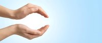 Two cupped hands in protective gesture against soft blue sky background symbolizing care, protection, safety and support concepts for healthcare insurance.