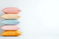 Colorful decorative pillows stacked vertically against white background, featuring pastel pink, peach, blue, and orange tones, creating minimal home decor composition.