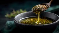Golden honey dripping from wooden spoon into black bowl with herbs and spices, dramatic dark food photography on green background, macro shot.