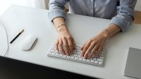Professional businesswoman typing on wireless keyboard at modern white desk workspace with documents and smartphone for office productivity.