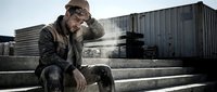 Exhausted male construction worker in dirty work clothes and hard hat sitting on steps at industrial site, head in hand, looking stressed.