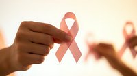 Hand holding pink ribbon symbol for breast cancer awareness campaign with blurred supporters in background creating unity and hope for medical research.